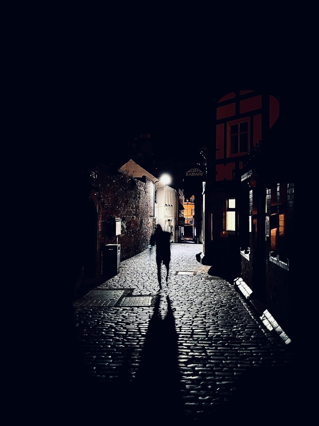 Lone silhouette walking through a narrow cobblestone street at night